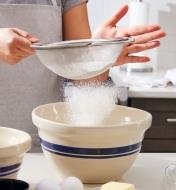 Sifting flour over a mixing bowl