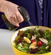 Personne aspergeant une salade avec le vaporisateur d’huile