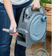 A gardener carries the manual hose reel while holding the end of the hose in their other hand