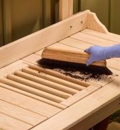 A gardener uses a brush to sweep soil from the tabletop down into the reservoir