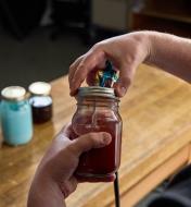 The Air-Powered Spray Gun being screwed onto to a mason jar, with two other jars on a workbench in the background