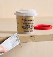 A putty knife being used to apply filler to the edge of an MDF board