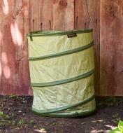 The Fiskars Kangaroo 30 Gallon Pop-Up Tote sitting on dirt in front of a large piece of wood