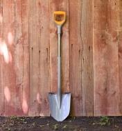 An orange-handles Fiskars digging shovel leaning against fence boards