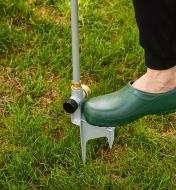 A gardener uses their foot to press the base stake of a telescoping sprinkler into the ground