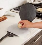 Personne déposant une boule de pâte sur une feuille de papier parchemin placée sur la plaque inférieure d'une presse à tortilla