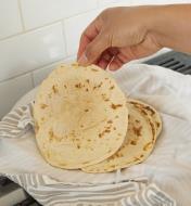 A homemade tortilla being lifted off a kitchen towel