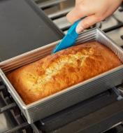 Using a knife to loosen fresh-baked bread from the loaf pan