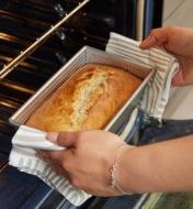 A baker removes the loaf pan with baked bread in it from an oven