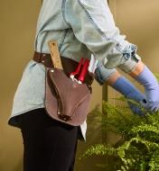 Personne munie d’un porte-outils de jardinage en cuir à la taille prenant soin d’une plante