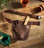 The completed gardener’s leather tool belt sits on a wood surface with garden tools placed in the pouch