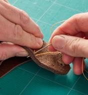 Using a needle and thread to stitch a piece of leather