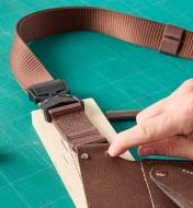 Personne fixant une ceinture-sangle à un porte-outils de jardinage en cuir avec des rivets