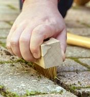 A hand-held weed brush being used to clear weeds between patio stones