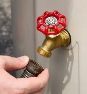 A hose is connected to the threaded brass faucet near the bottom of the rain barrel