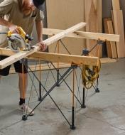 A man cuts lumber on a saw trestle made from two-by-fours set across a Bora Centipede table