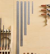 Four stainless-steel cabinetmaker’s rules of varying sizes hung on a wall.