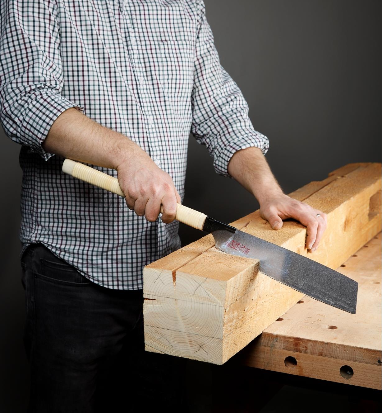 Personne effectuant une coupe dans une épaisse poutre en bois avec la scie kataba convexe à tronçonner