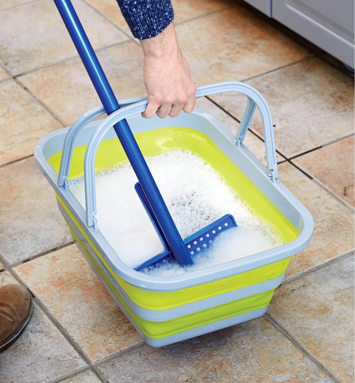 Rinsing a mop in a collapsible tote filled with soapy water.