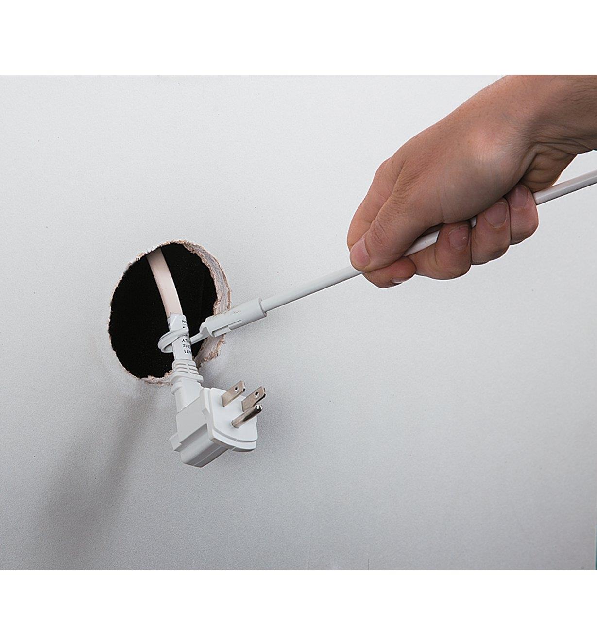 Using the hook to pull the plug end of the cord through the hole in the wall