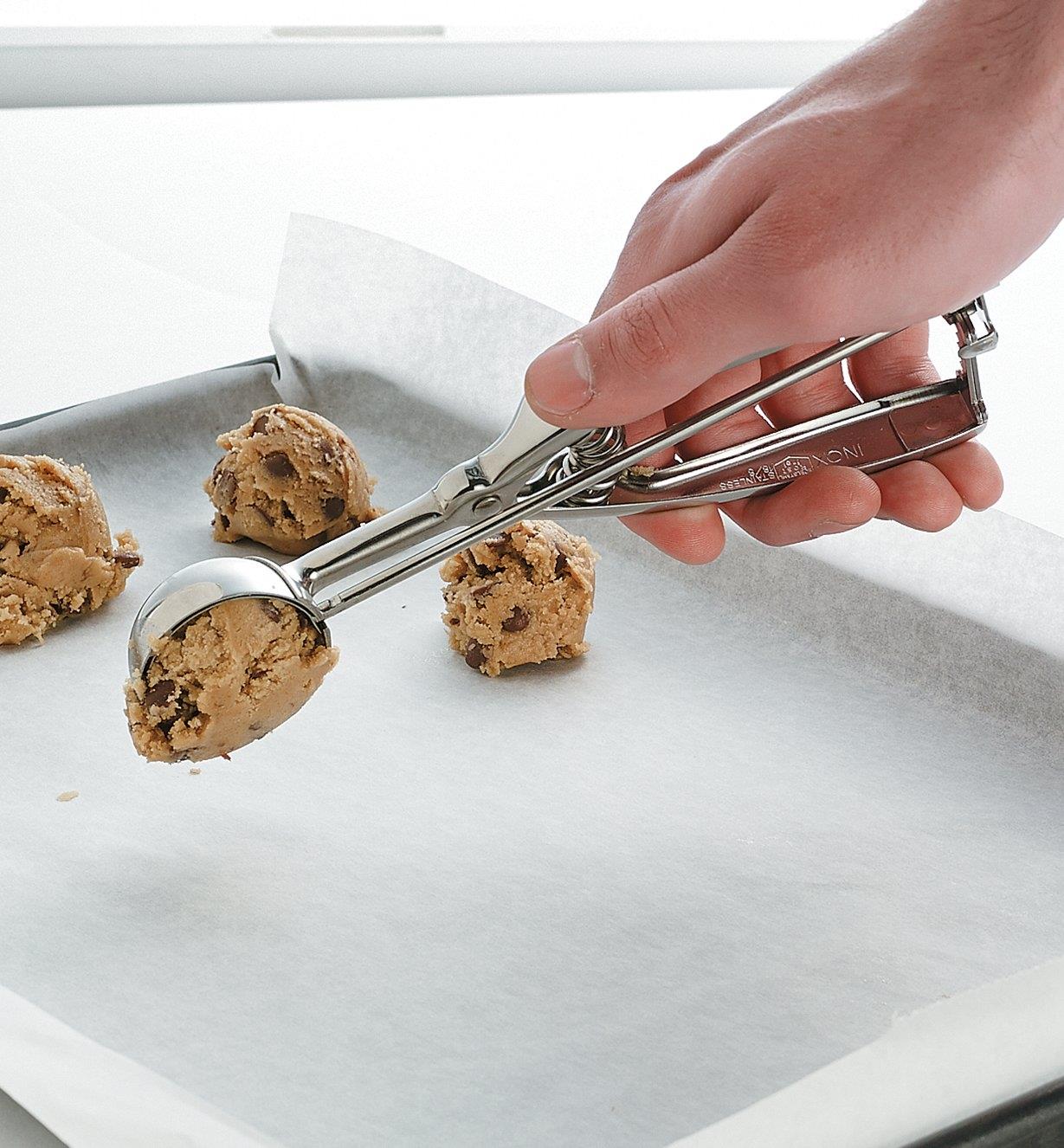 Personne déposant une cuillérée de pâte à biscuits sur une plaque à biscuits tapissée de papier parchemin
