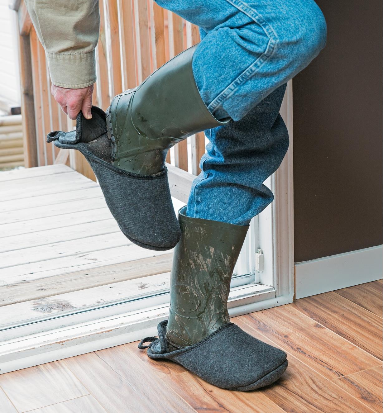 Man putting on second boot slipper over muddy boot before coming inside