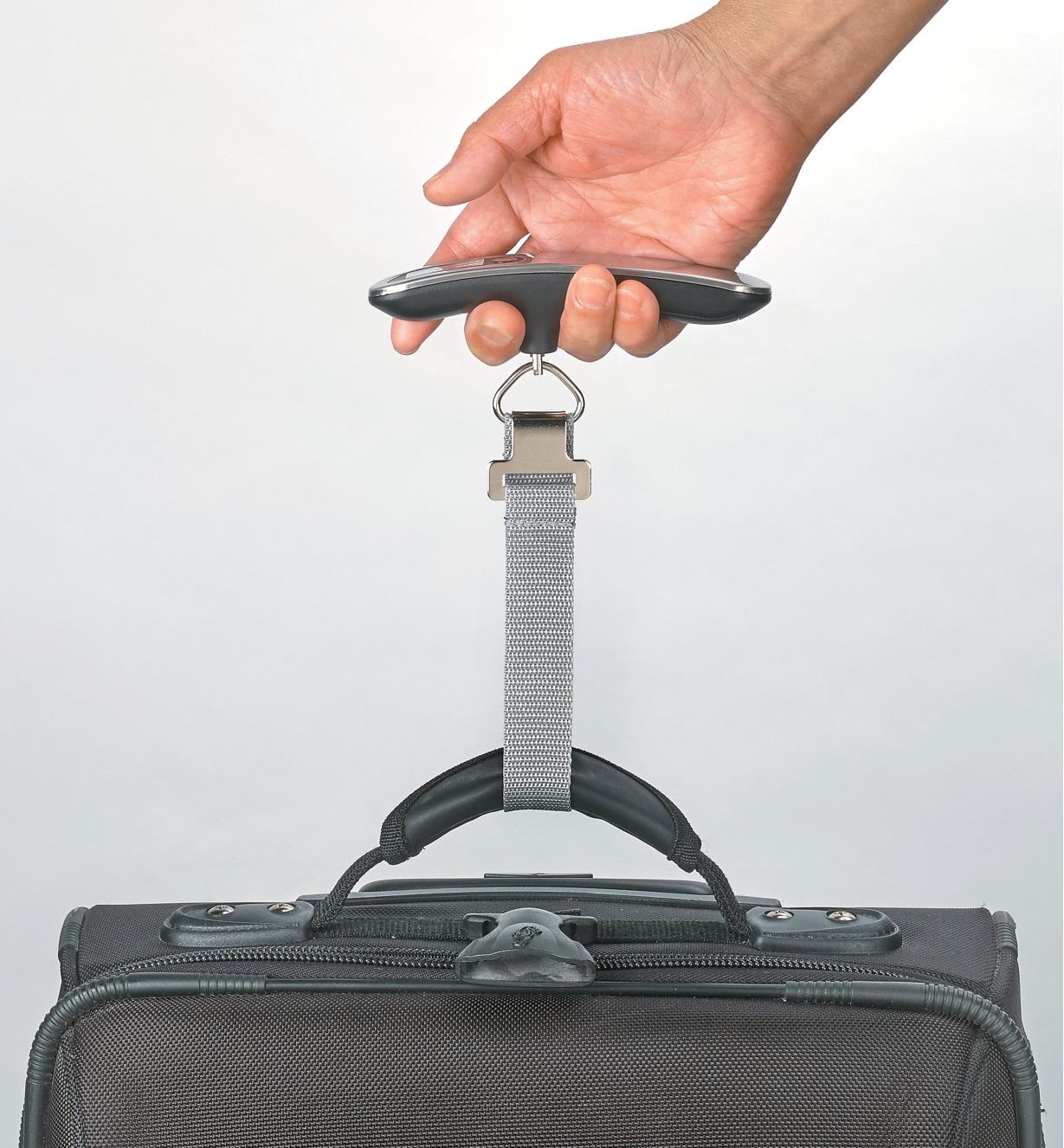 Personne pesant une valise à l'aide d'un pèse-bagage numérique