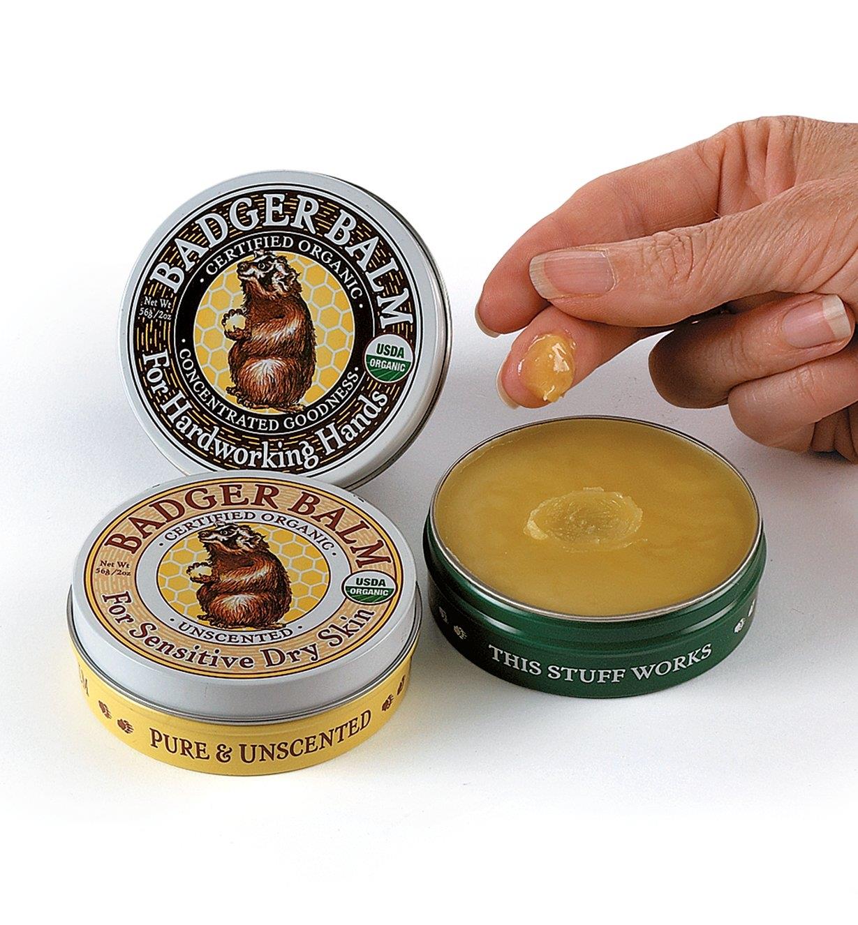 Badger Balm, both scented and unscented, beside a hand with balm on the fingertips