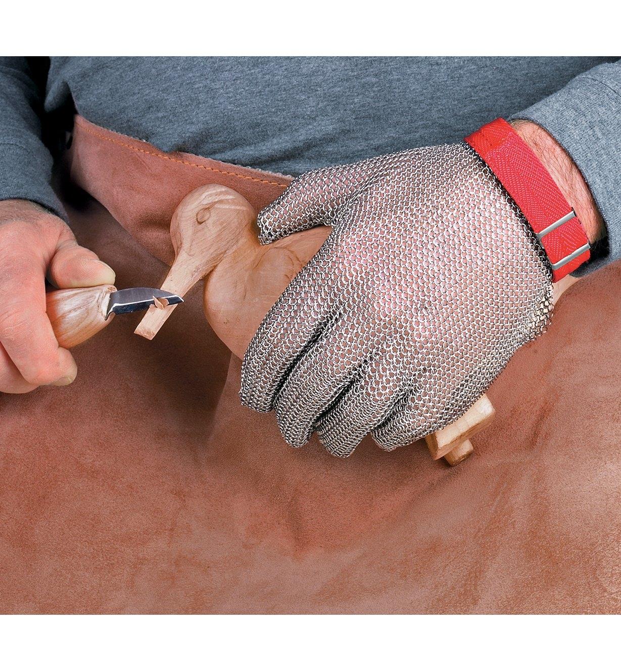 A person carves a wooden bird while wearing a Carver's Chain Mail Glove