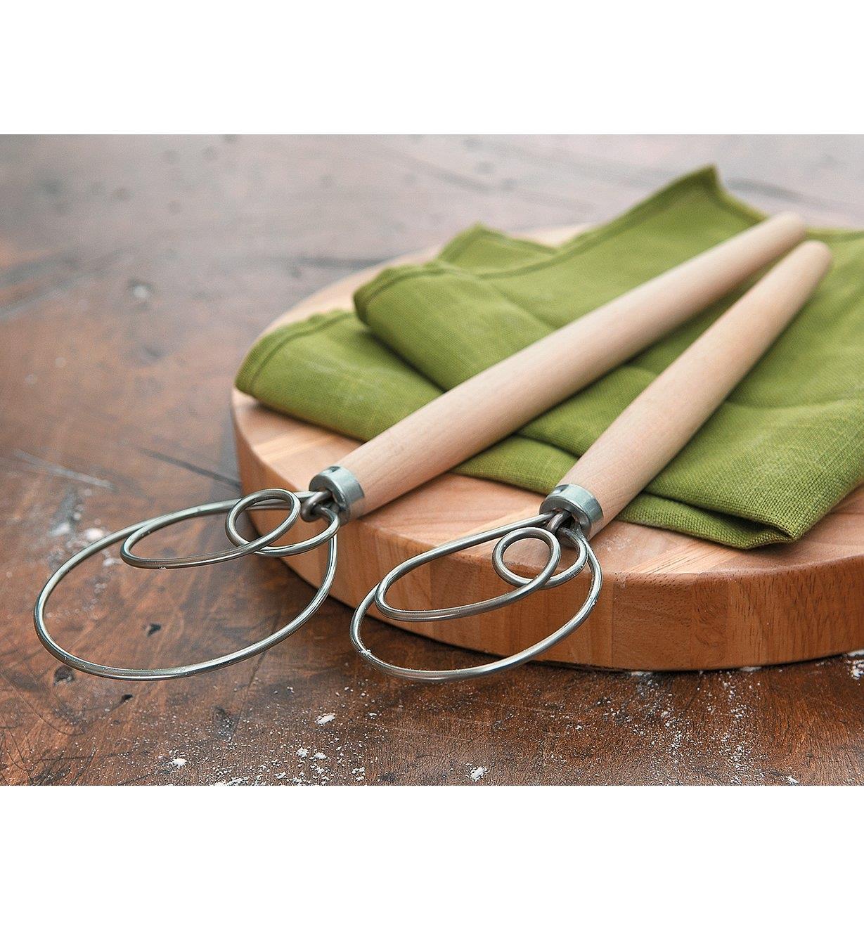 Both sizes of Danish Dough Whisks lying across a cutting board