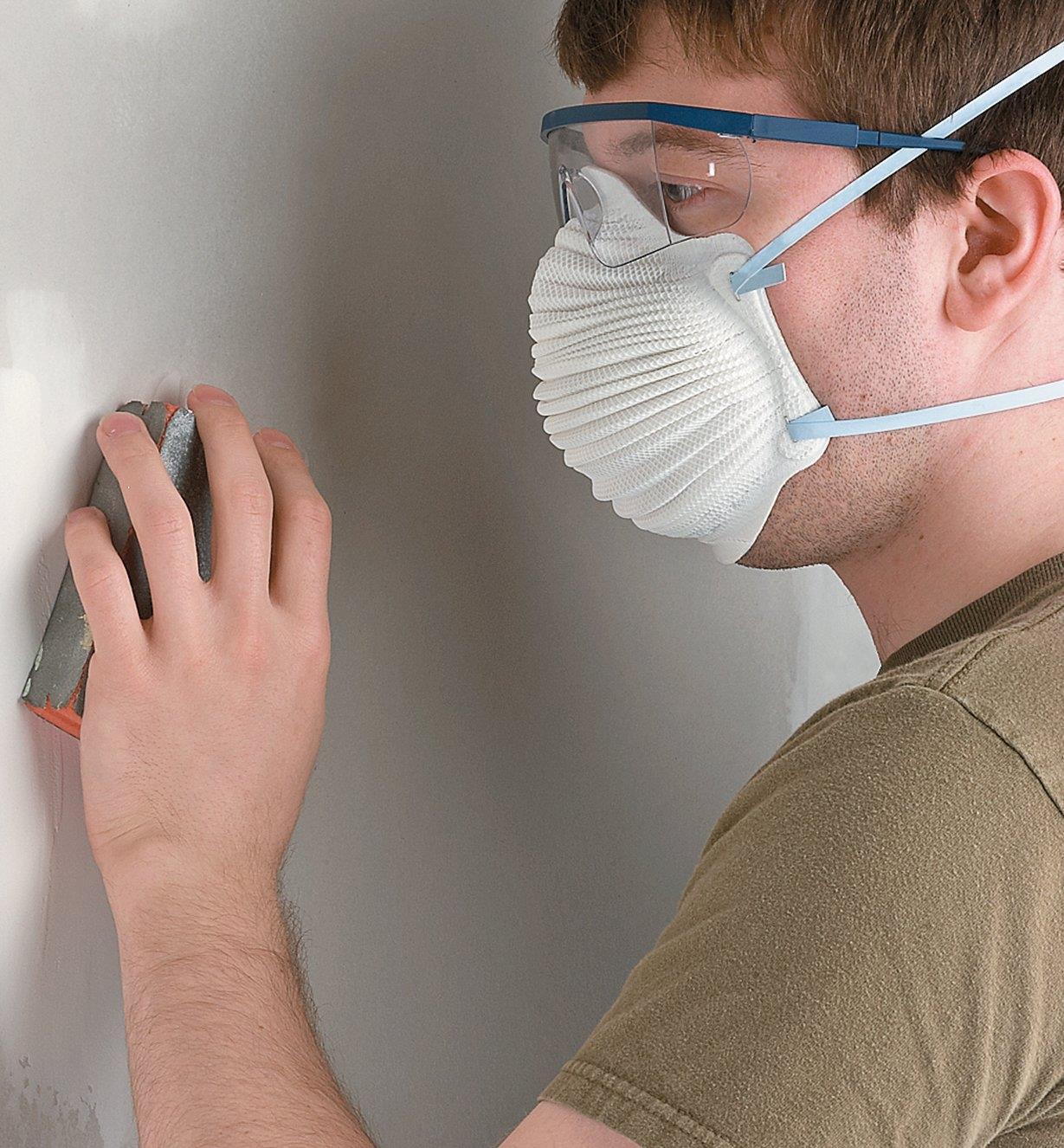 A person wears an Airwave disposable dust mask while sanding a wall