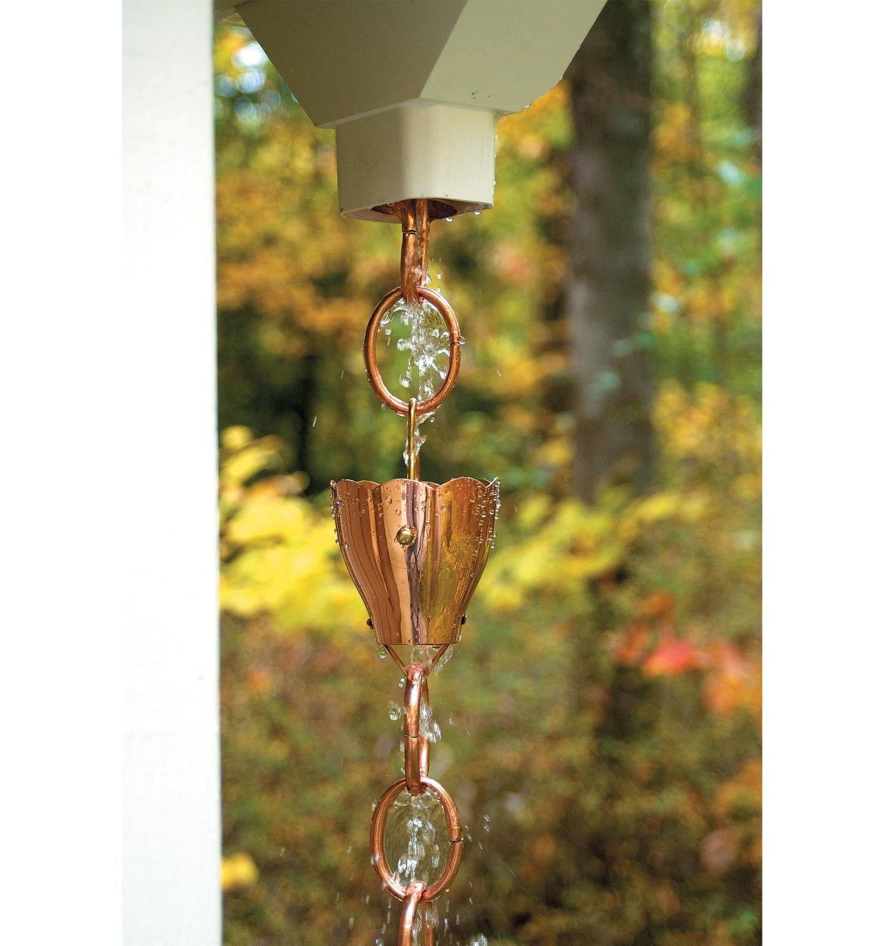 Water from a downspout opening cascades through the fluted funnels on the copper rain chain