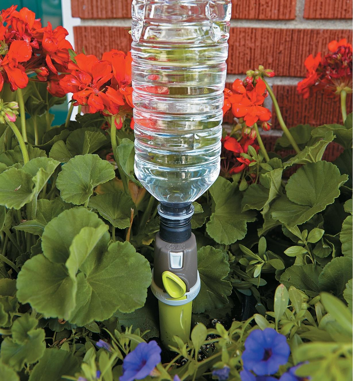 Adjustable-Flow Drip Spike with a plastic bottle attached inserted in a flower garden