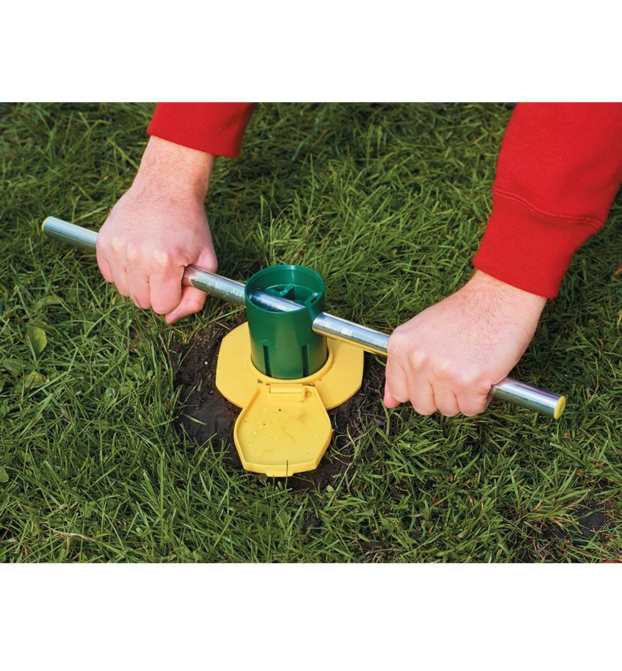 Installing the ground screw anchor by twisting it into the ground using a metal bar