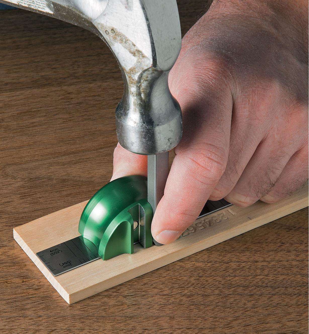 Tapping a stamp with a hammer to mark a letter in wood, using the spacing guide