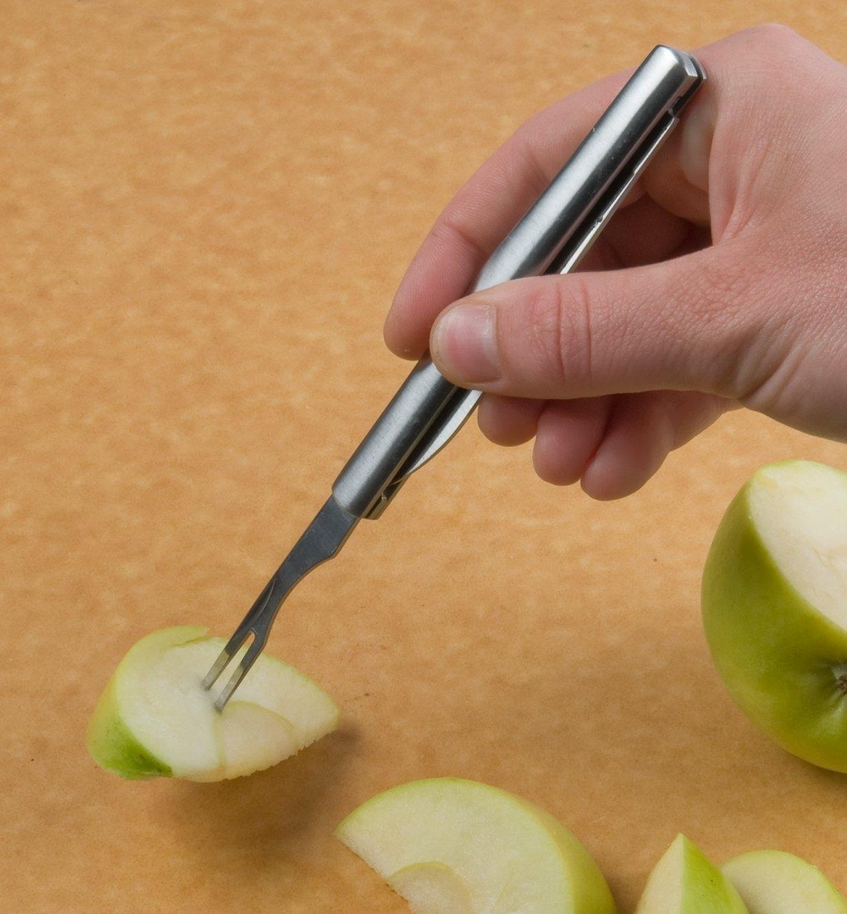 Personne piquant une tranche de pomme avec la fourchette d'un couteau à fruits pliant