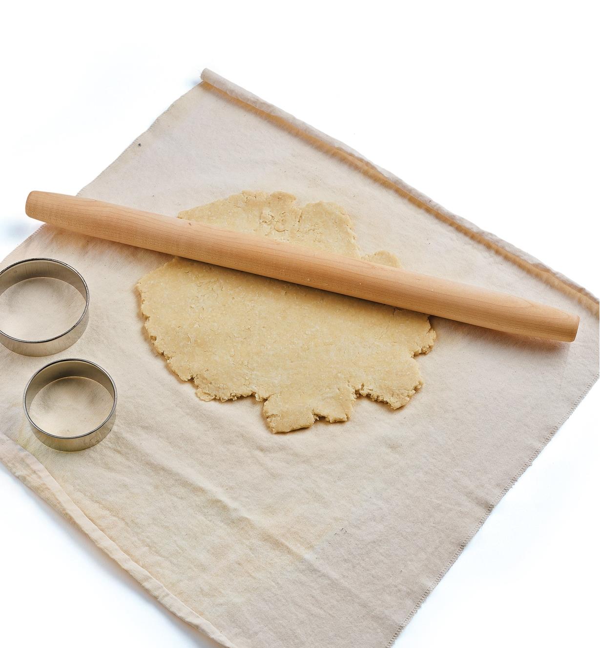 The French-Style Rolling Pin, some rolled dough, and two pastry cutters sit on top of a pastry cloth 