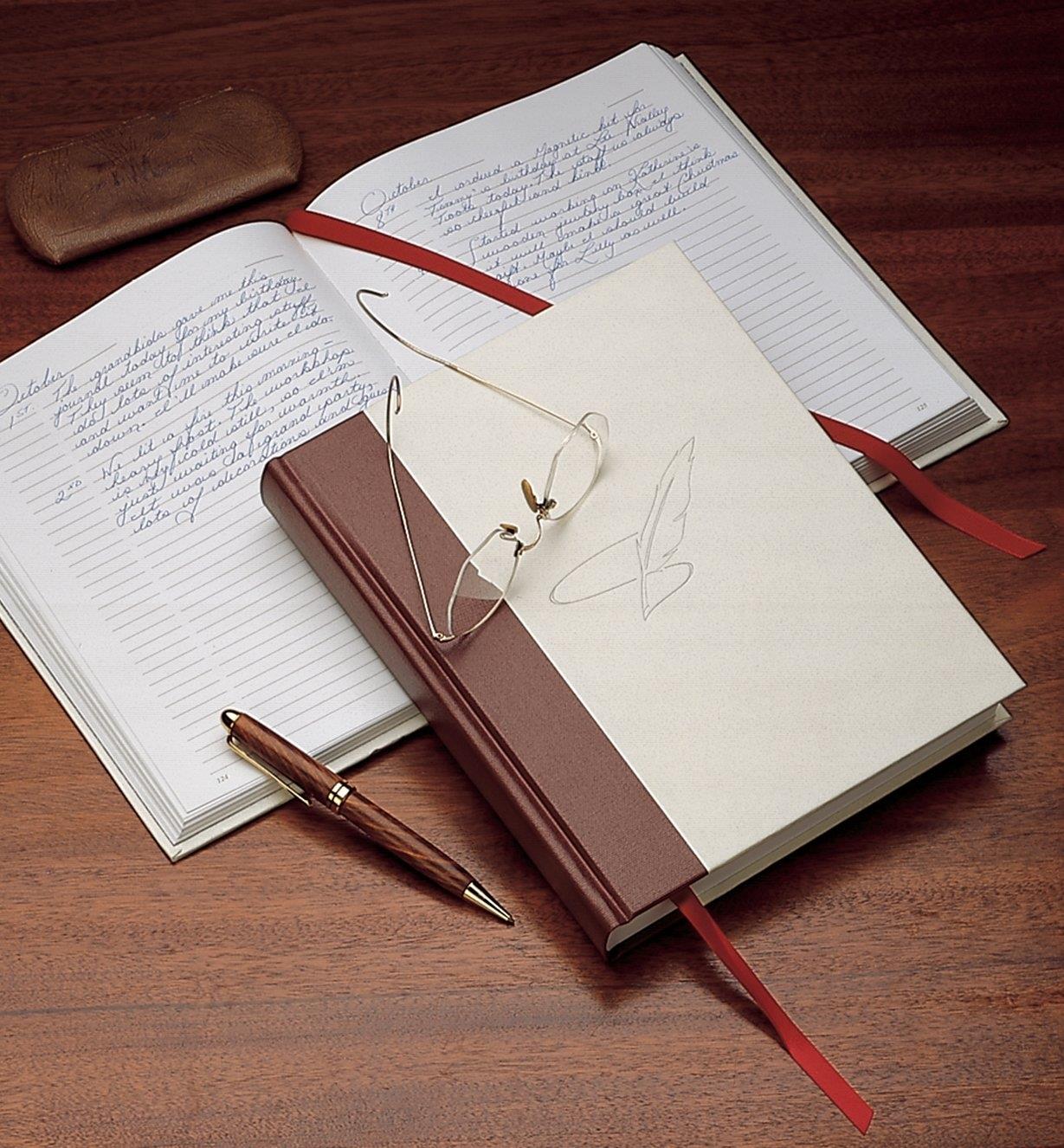 A pair of glasses and a pen resting on a closed Everyman's Journal lying on an open journal with writing on the pages