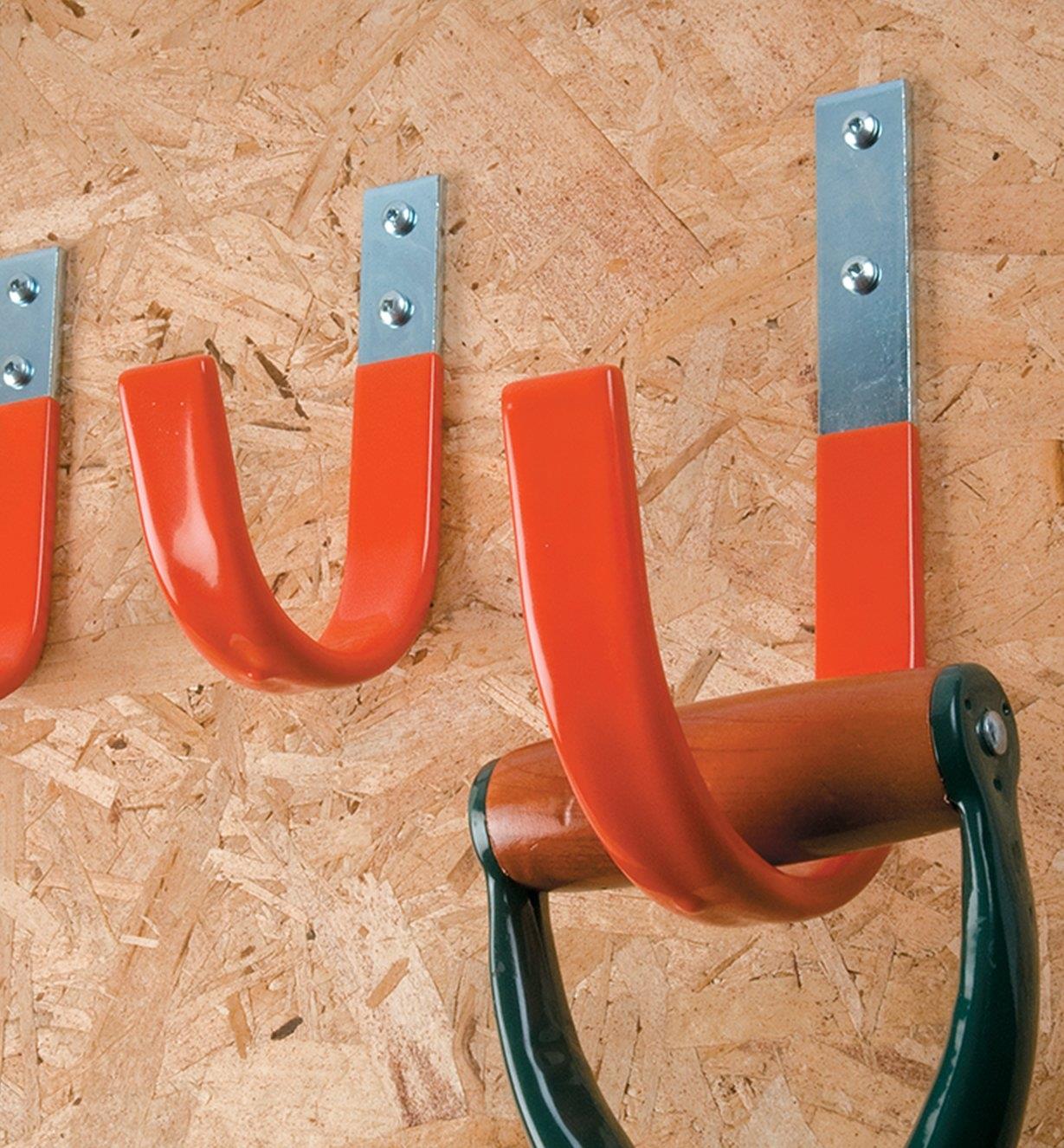 Several Heavy-Duty Strap Hooks mounted to a garage wall, one of them holding a D-handle tool