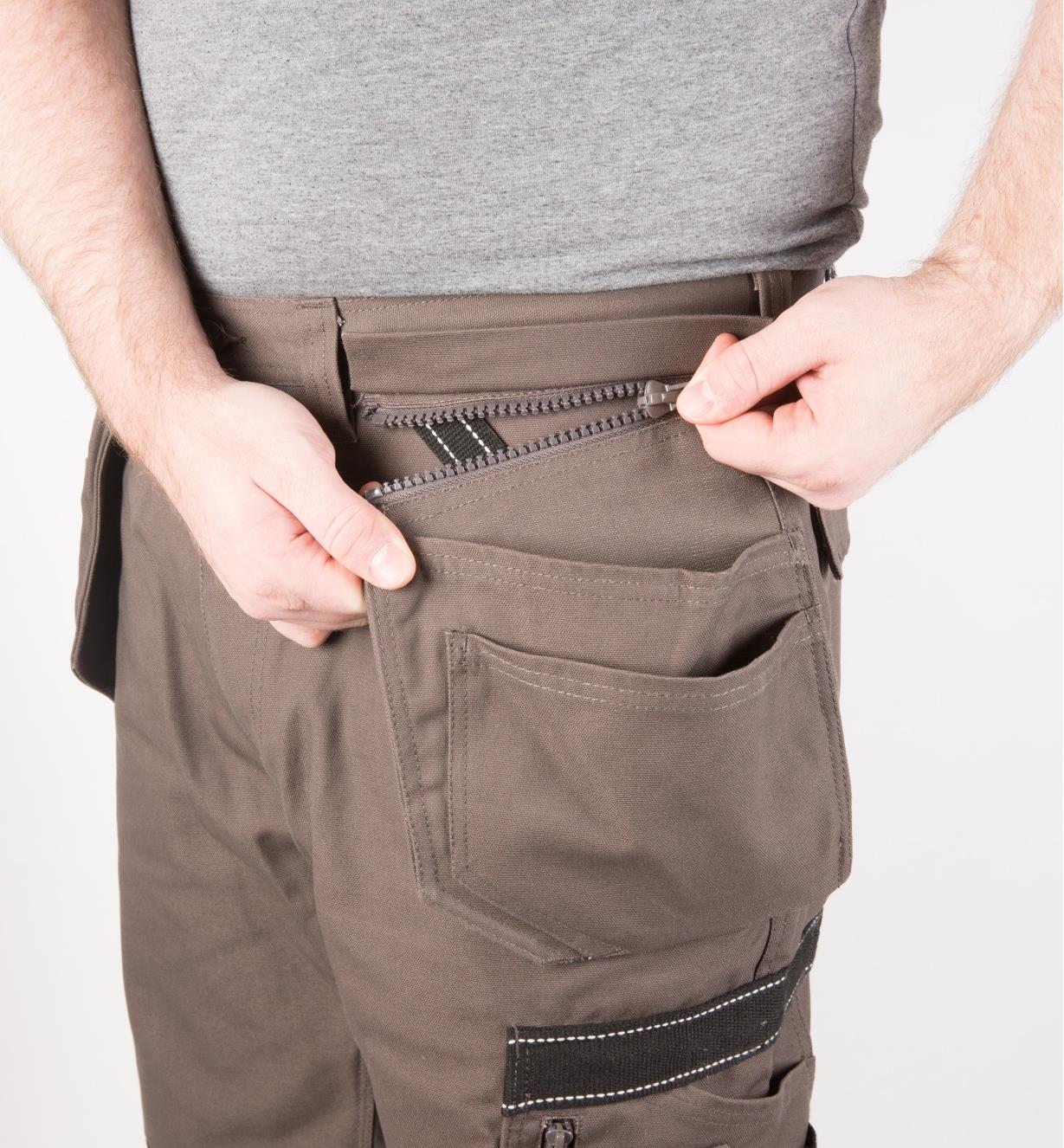 A man wearing gray work pants unzips one of the side pouches