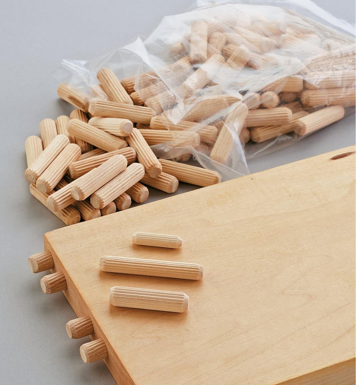 A shelf with dowels installed in the end and various dowels sitting on top and beside it