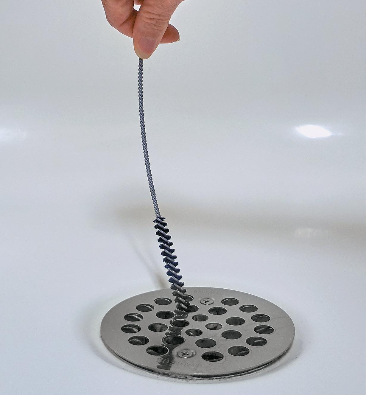 The drain-cleaning brush being inserted into a shower drain cover