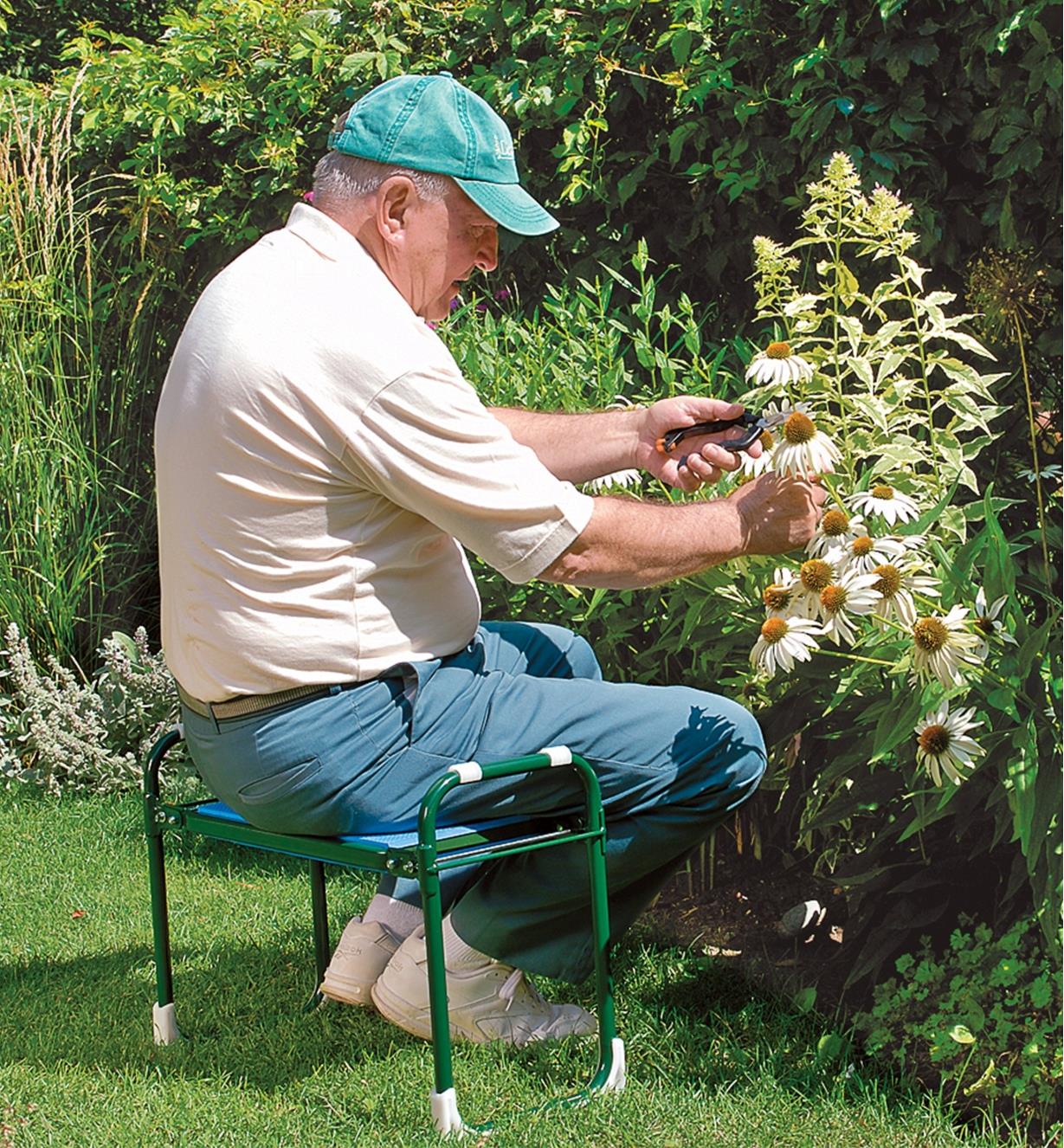 A man sits on the folding kneeler stool while cutting flowers