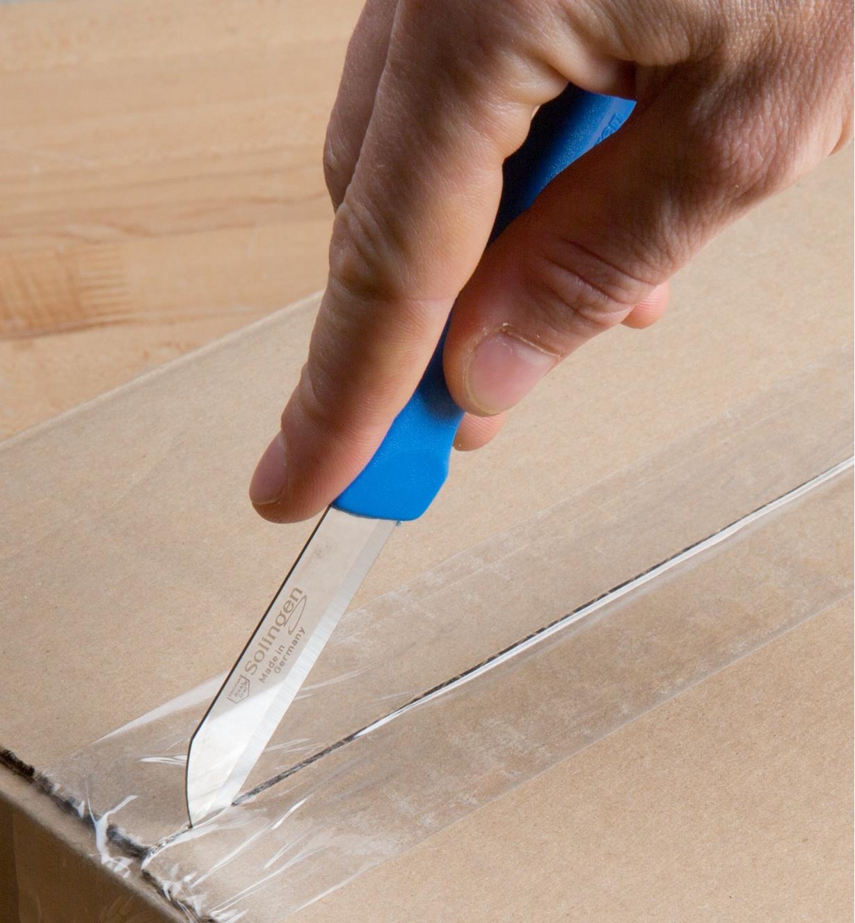 Using a paring knife to cut packing tape on a cardboard box