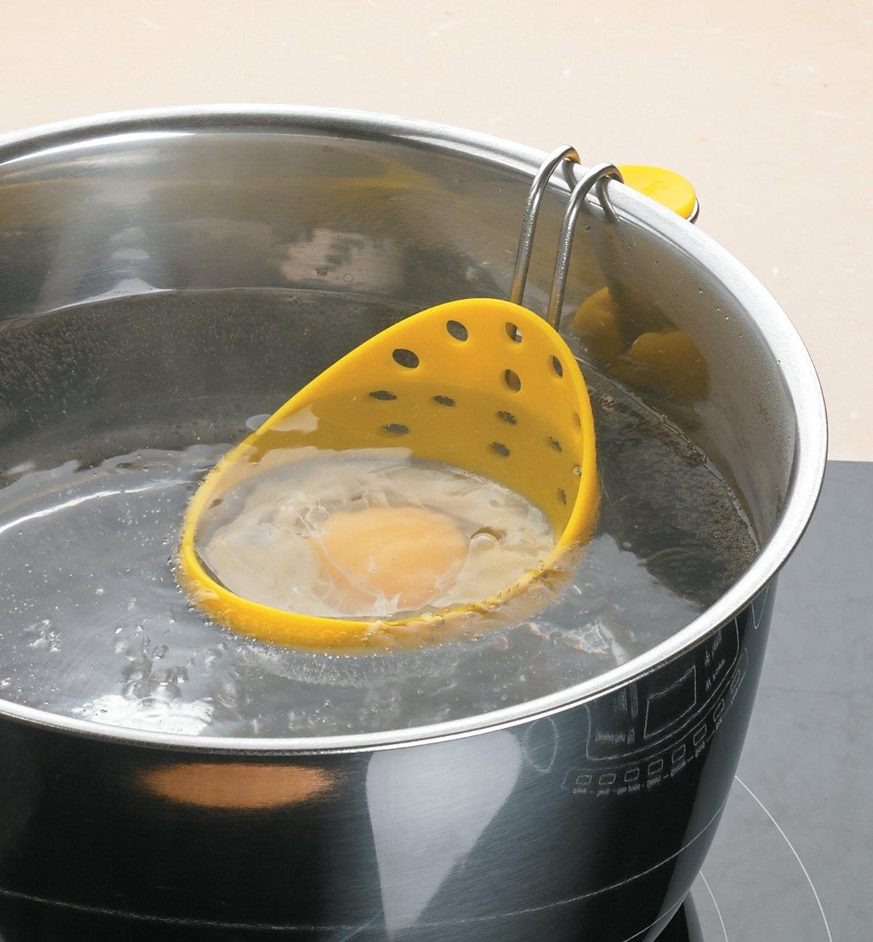 Œuf cuisant dans une casserole d'eau bouillante à l'aide d'une pocheuse à œufs
