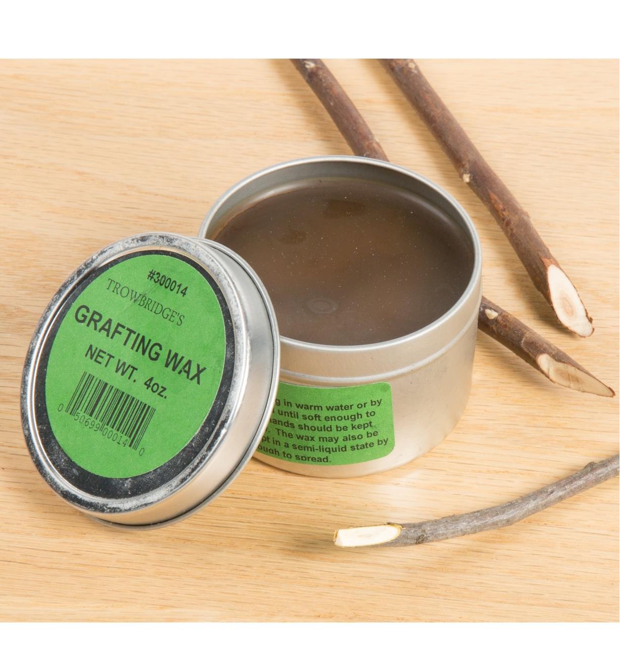 An open tin of grafting wax next to a several twigs