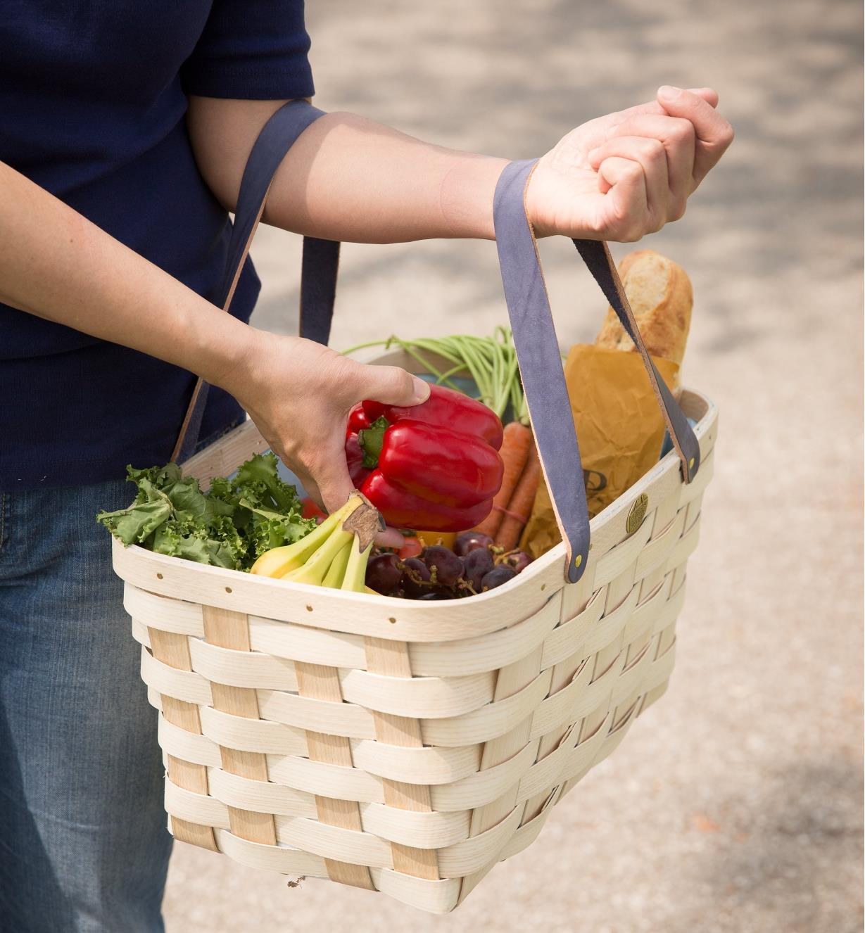 A woman holds a Handwoven Basket Tote filled with produce and a baguette
