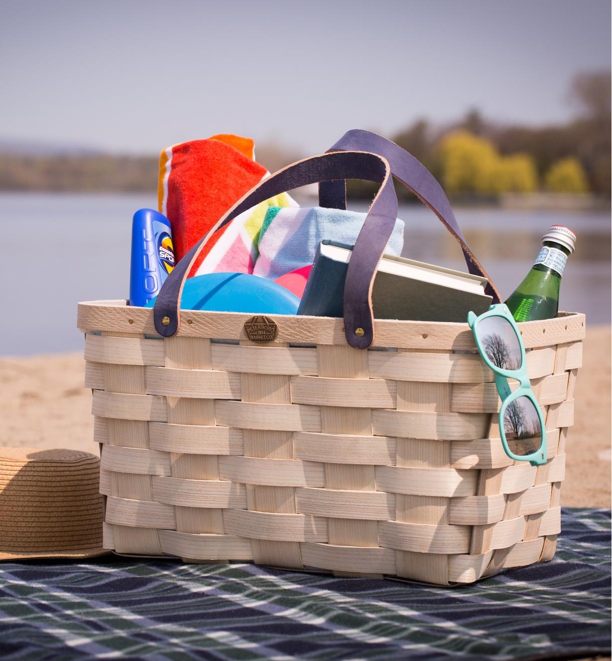 Handwoven Basket Tote on a blanket on a beach, holding towels and other beach accessories