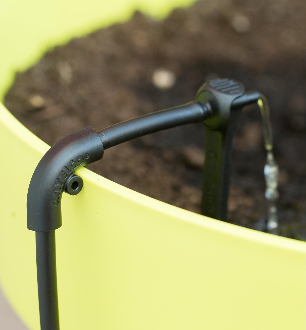 Clip-on elbow fitted onto irrigation hose and mounted to the edge of a planter