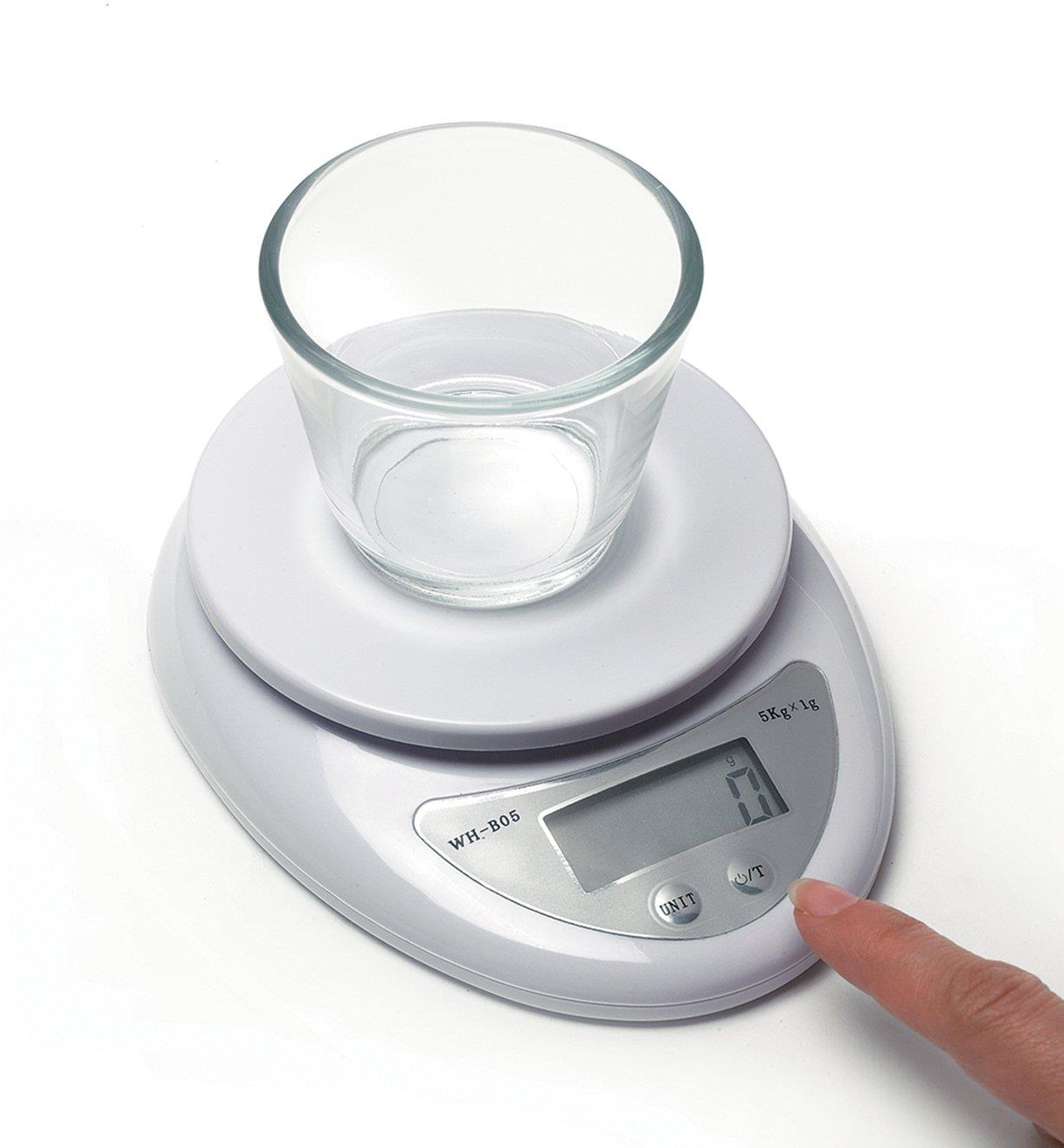 Personne réglant à zéro la tare d'une minibalance de cuisine numérique sur laquelle repose un petit bol en verre